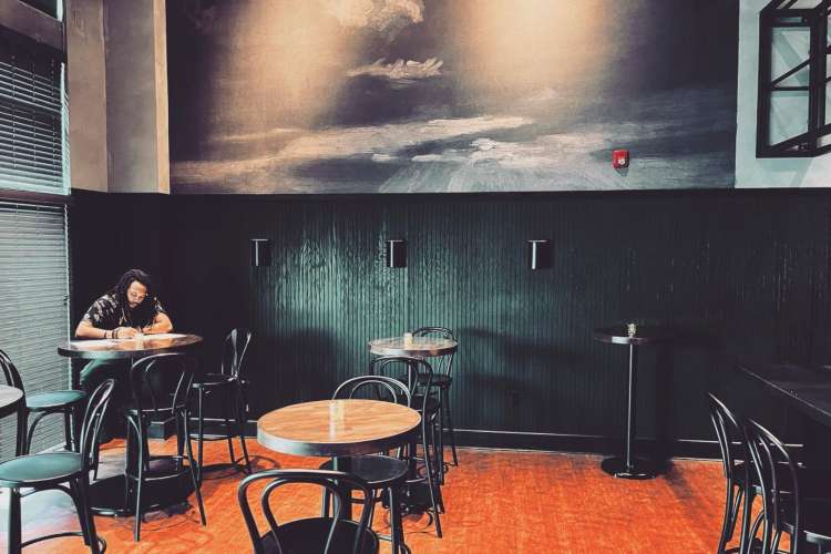 man in an atmospheric cafe setting with a painting on the upper wall