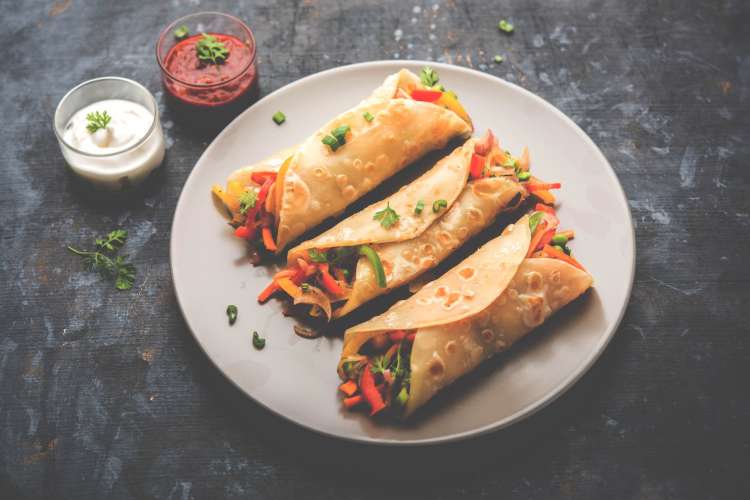 three Indian kathi rolls on a plate with red and white sauces on the side