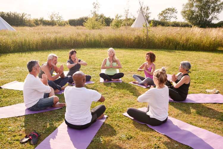 a diverse group sits in a circle in a garden outdoors and meditates