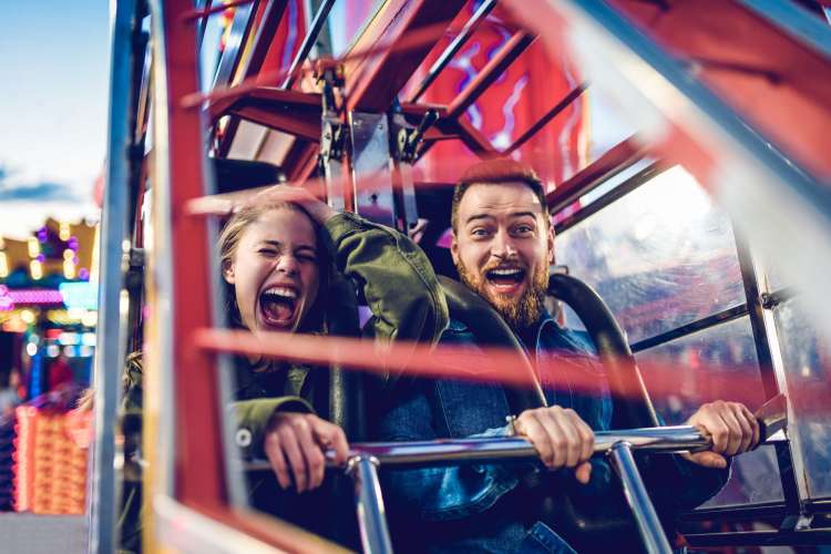 a woman screams happily on a rollercoaster while her male partner grins widely into the camera