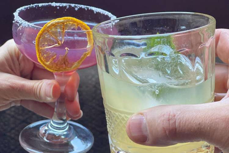 closeup of two people toasting with colorful cocktails
