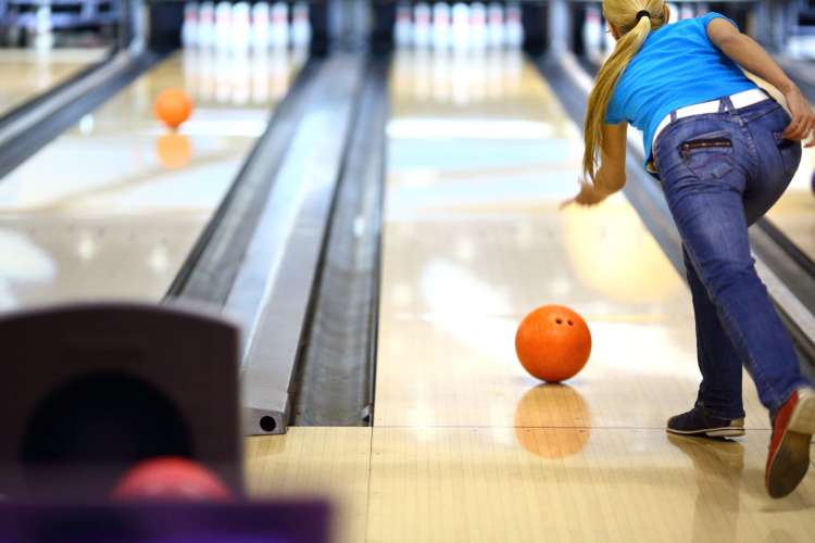 a woman with a long ponytails grows a bowling ball in an alley