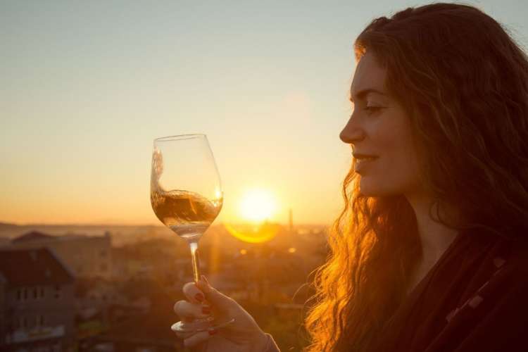 a smiling woman holding a wine glass against a sunset