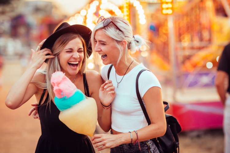 a female couple laughs and shares cotton candy at a festival