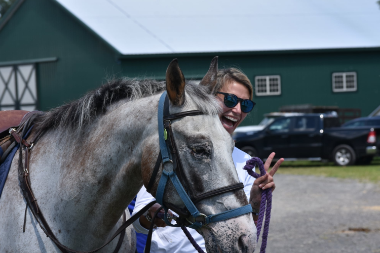 a woman smiling behind a gray horse