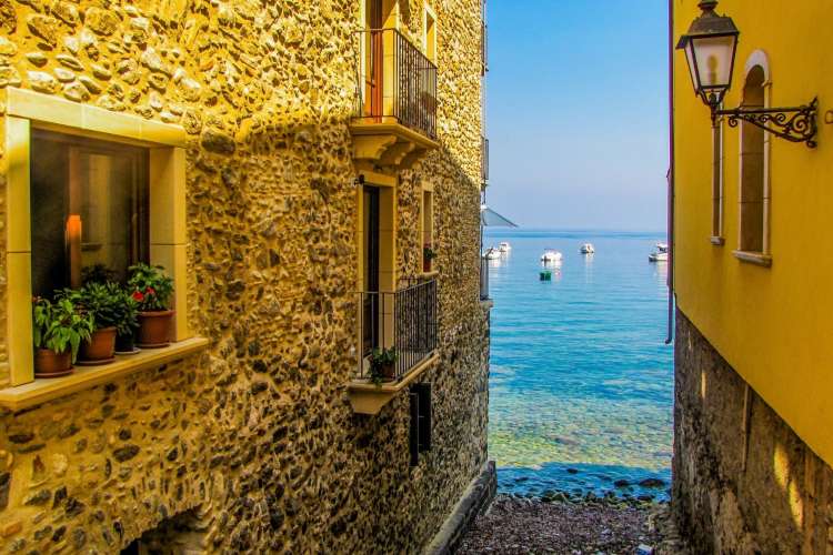 looking out at the blue sea from a narrow alley between two vibrant yellow buildings