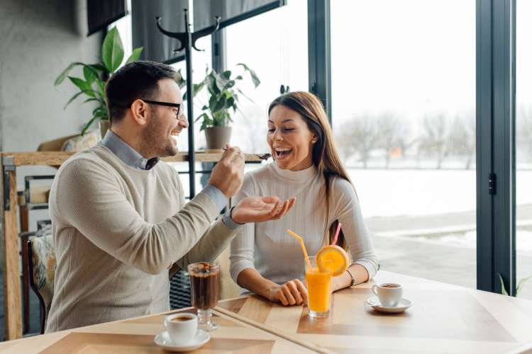 A man feeding a woman dessert at a bright restaurant, which is a great one-year anniversary date idea