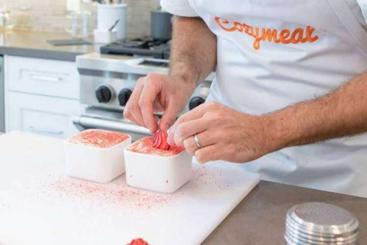 a chef in a Cozymeal apron garnishes a dessert with fresh fruit