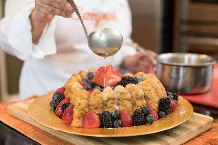 a chef in a Cozymeal apron pours sweet sauce on a cake made of lady fingers