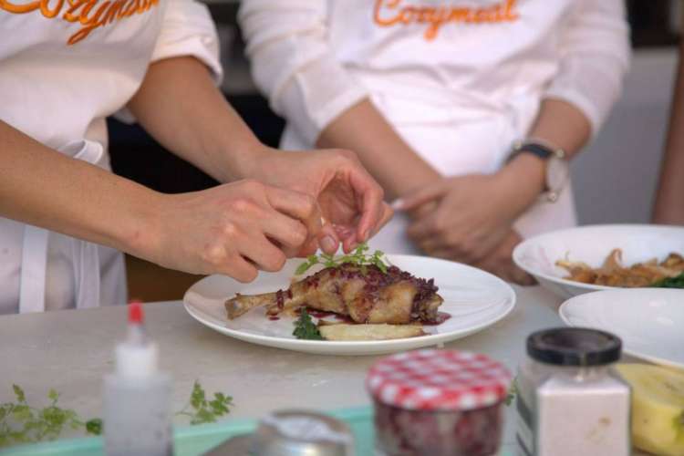 a chef in a Cozymeal apron garnishing a plate of chicken