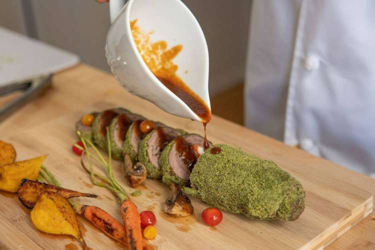 a chef pouring a dark sauce over a sliced vegetable loaf