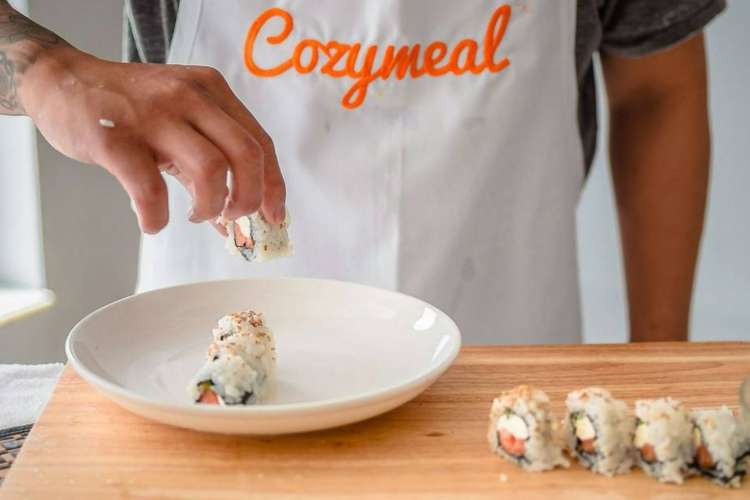 a chef wearing a Cozymeal apron prepares a California Roll. 