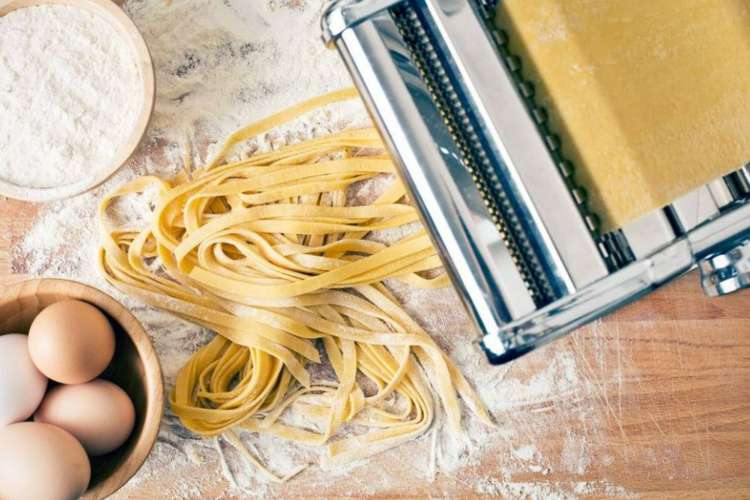 raw pasta sitting in a pasta maker on a flour-covered table