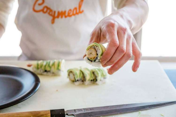 a chef in a Cozymeal apron preparing a sushi roll