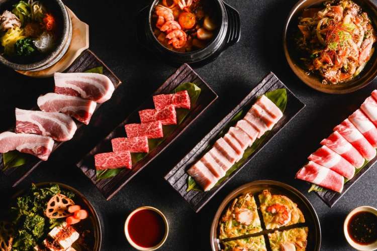 plates of uncooked meat among colorful vegetables and sides