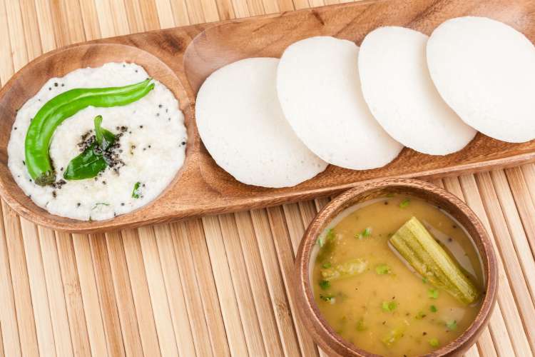 a bowl of sambar next to idli, savory rice cakes