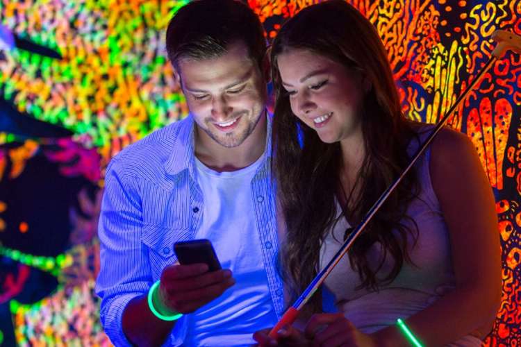 two smiling people on a date at a putting range look at a cellphone