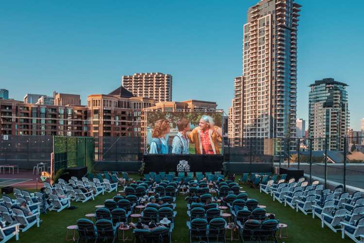 guests watching a big outdoor movie screen atop a roof in nyc 