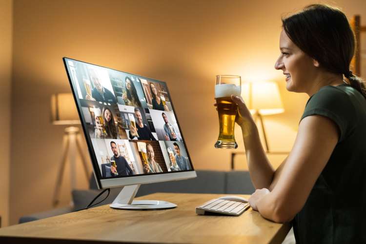 a woman holding a beer and smiling at a screen full of people