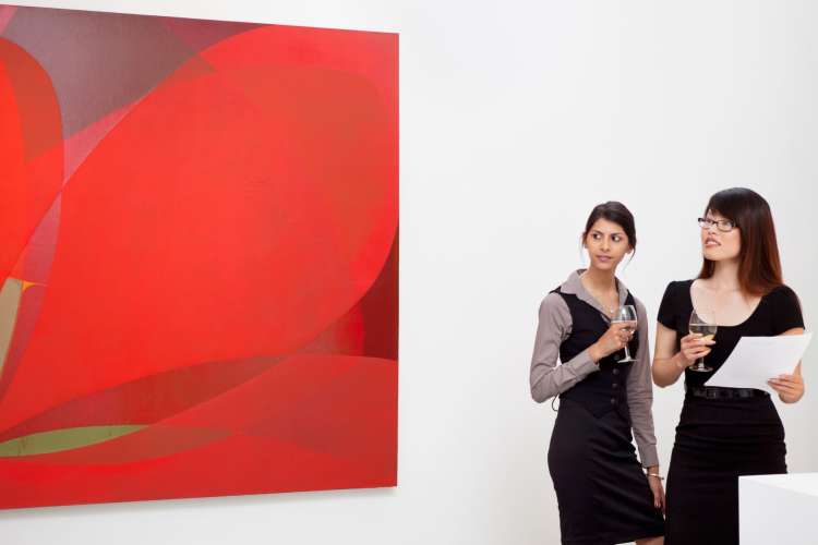 a couple holding champagne glasses look at a painting in a gallery