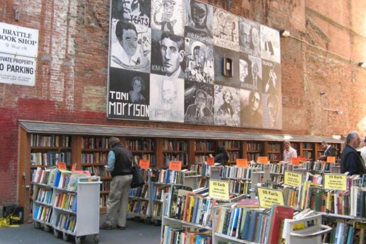 outdoor scene of used books for sale in front of a Toni Morrison mural on a brick building