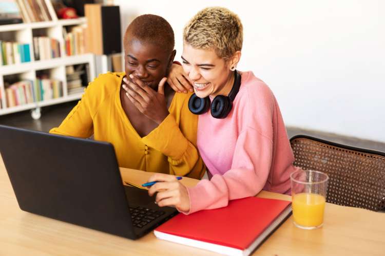 two women laughing at something on their laptop