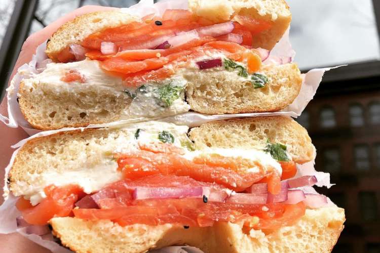 a bagel sandwich with tomato, onions, and chive cream cheese