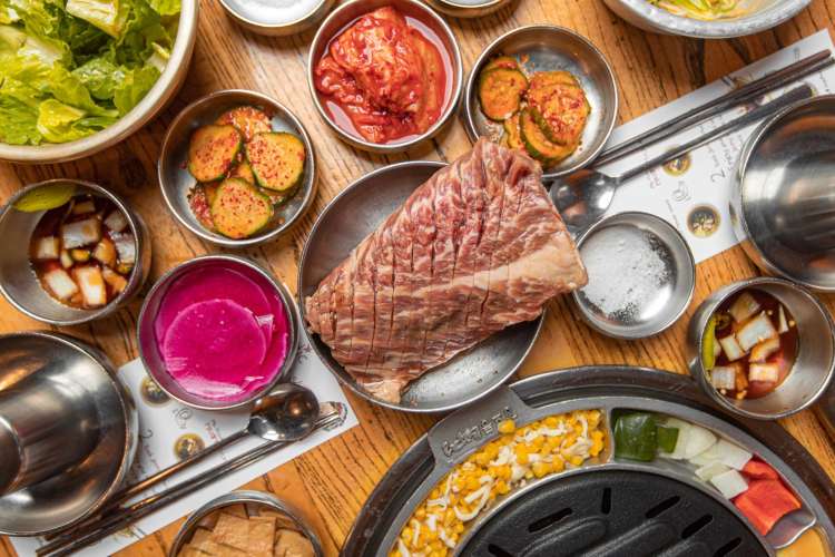 a table of meat, sides, and vegetables at a Korean barbecue