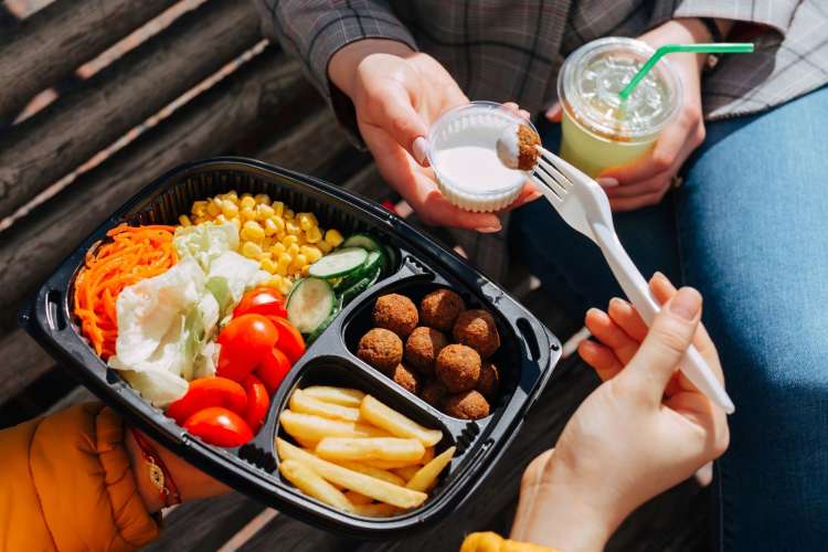 two people sharing veggies and falafel on a bench