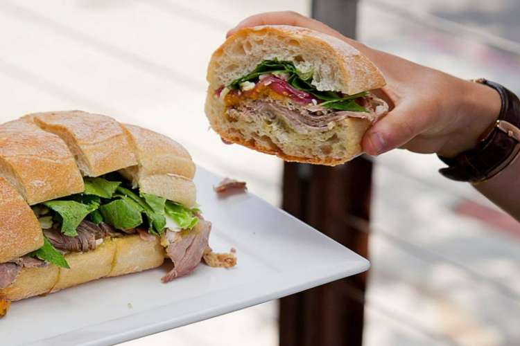 someone takes a piece of a deli sandwich from a plate on a food tour