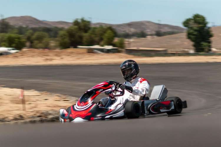 a driver in red jacket and black helmet drives a race car outside