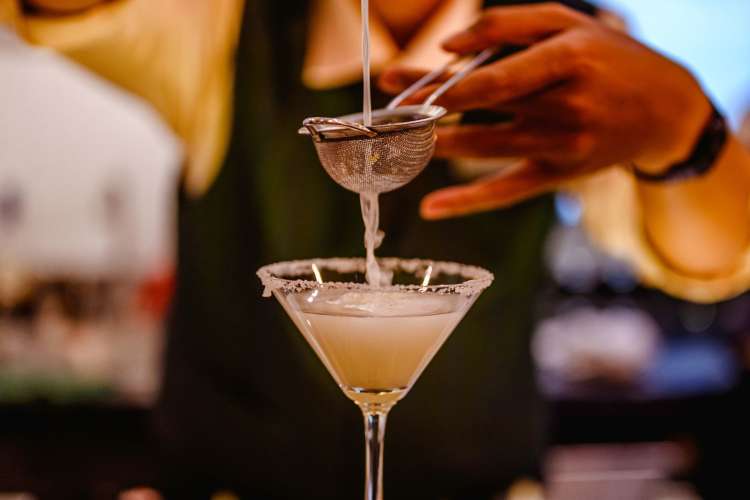 a mixologist uses a strainer to prepare a margarita