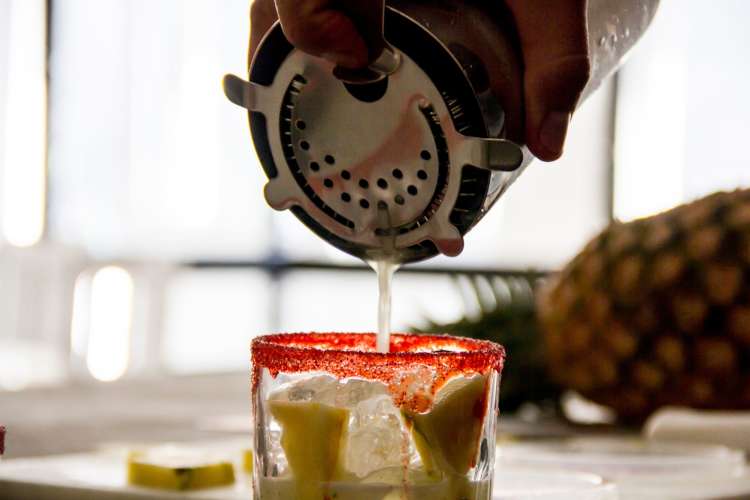 a bartender straining ingredients into a margarita on the rocks