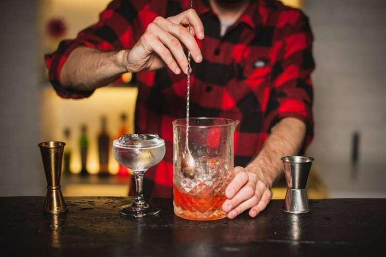 a bartender stirs the ice in a cocktail with a long-handled spoon