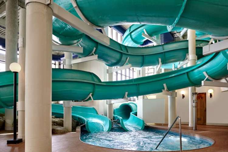 a twisting green slide above an indoor swimming pool