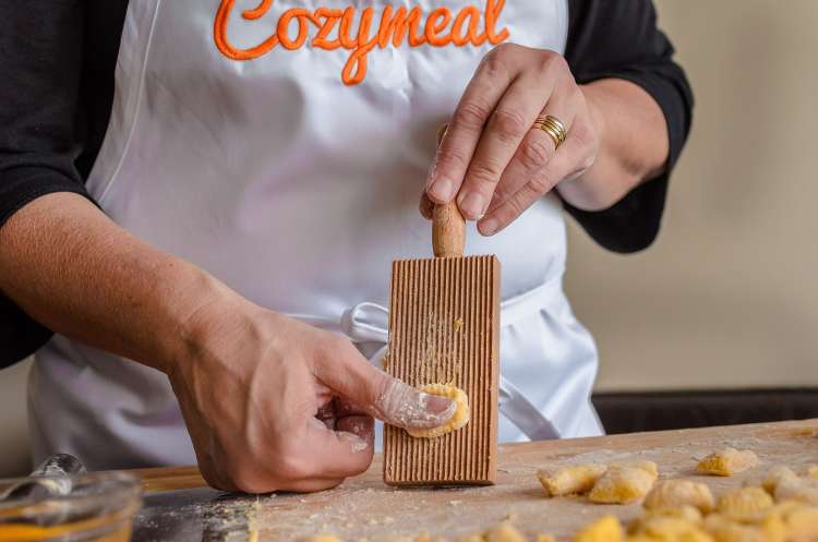 chef rolling gnocchi down a wooden gnocchi board