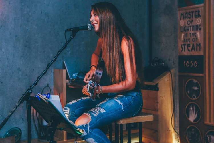 A woman sits on stage playing the guitar while singing