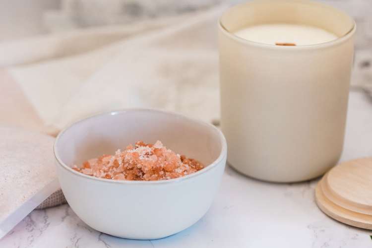 a white soy candle next to a dish of pink Himalayan sea salt