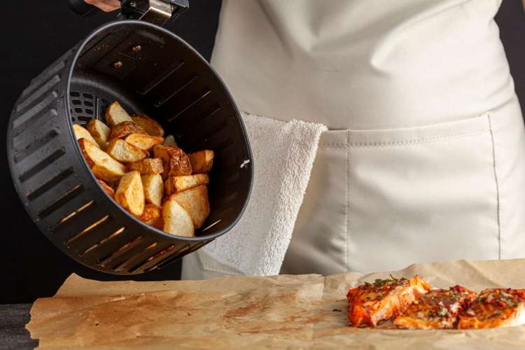 a chef pouring potatoes out of an air fryer basket onto a plate