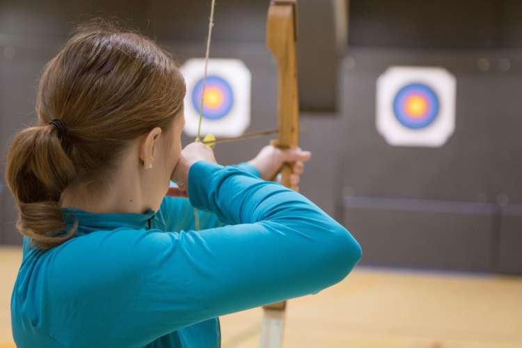 Woman pulling an arrow back in a bow, about to fire at a target