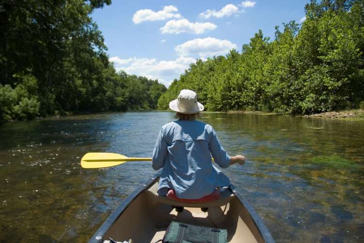 a woman sitting at the edge of a kayak paddling in a wooded river area