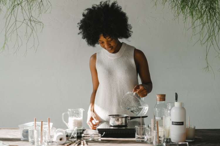 a woman pours liquid into a saucepan to make a candle