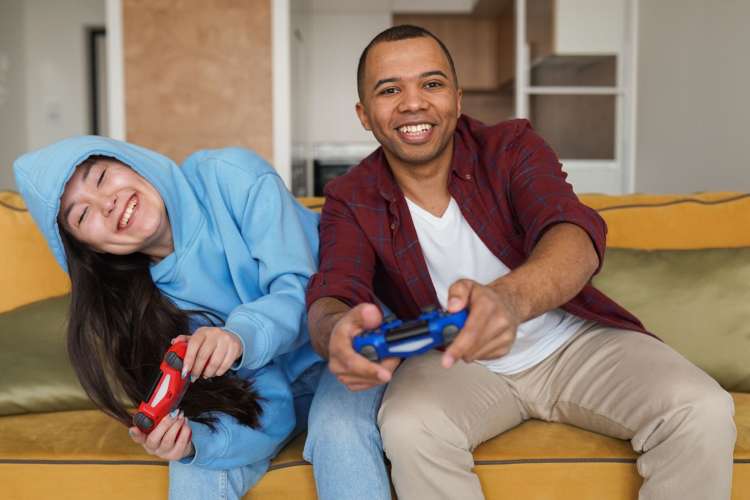 a couple playing video games and laughing on a sofa