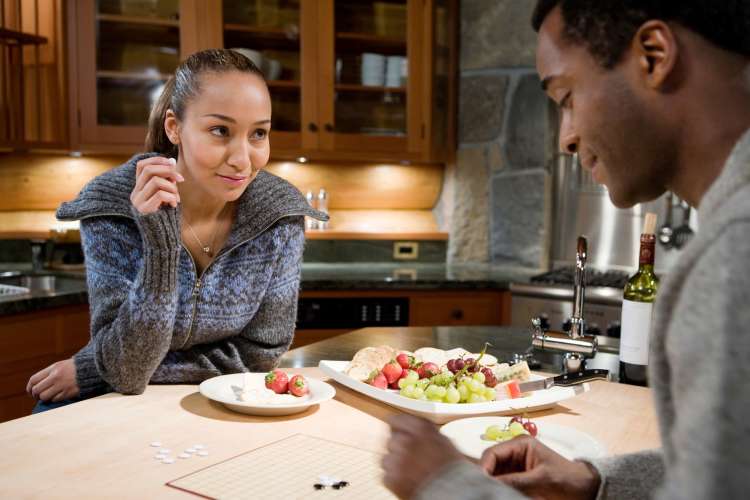 a couple plays a board game in their kitchen while snacking on fruit