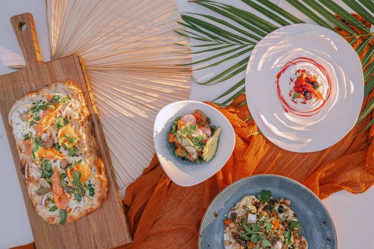 a spread of pizza, salad and other dishes on a beach-themed background