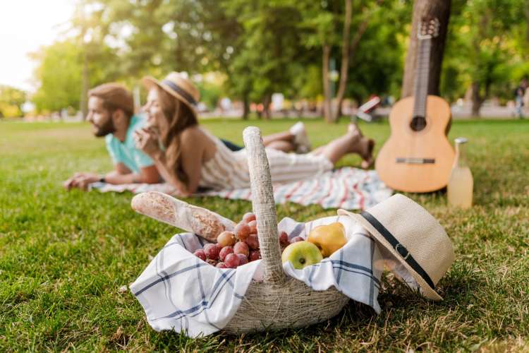 A basket of food in front of a guitar and a couple during a picnic date