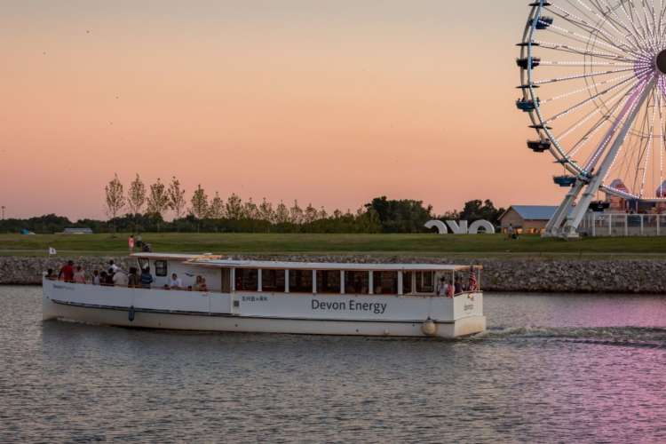 a ferry on the Oklahoma River at dusk, a Ferris wheel in the background