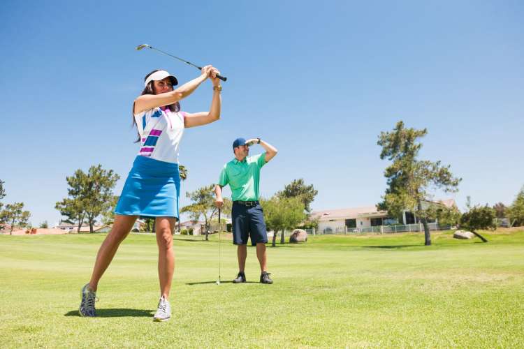 a woman hits a golf ball while a man looks on