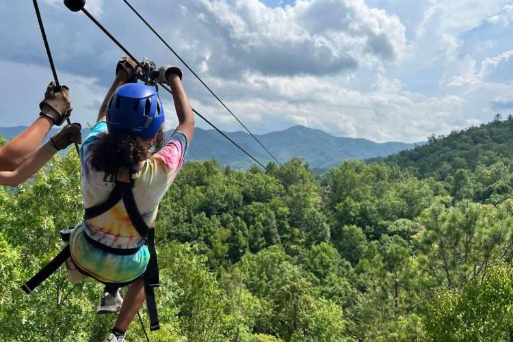 a woman tethered to a zip line about to glide down a steep line