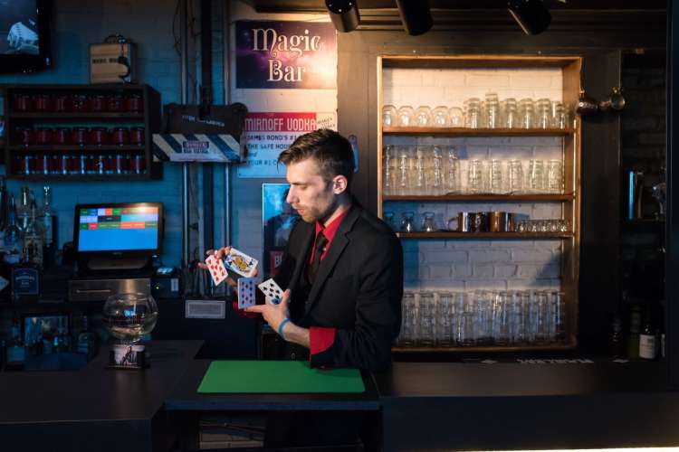 a bartender in a red shirt and black jacket shuffles a deck of cards